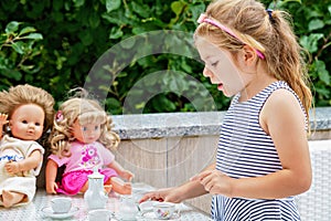 Little preschool girl playing with dolls. Happy excited child play tea party with toys. Role games for children