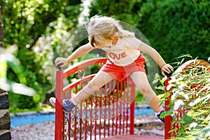 Little preschool girl playing on outdoor playground. Happy toddler child climbing and having fun with summer outdoors activity