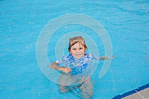 Little preschool girl playing in outdoor swimming pool in hotel resort. Child learning to swim in outdoor pool