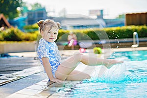 Little preschool girl playing in outdoor swimming pool by sunset. Child learning to swim in outdoor pool, splashing with