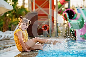 Little preschool girl playing in outdoor swimming pool by sunset. Child learning to swim in outdoor pool, splashing with