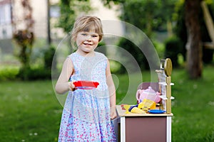 Little preschool girl playing with toy kitchen in garden. Happy toddler child having fun with role activity game