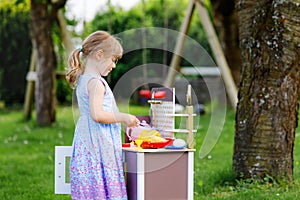 Little preschool girl playing with toy kitchen in garden. Happy toddler child having fun with role activity game