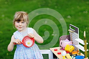 Little preschool girl playing with toy kitchen in garden. Happy toddler child having fun with role activity game