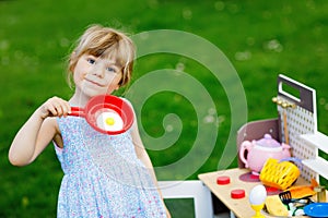 Little preschool girl playing with toy kitchen in garden. Happy toddler child having fun with role activity game