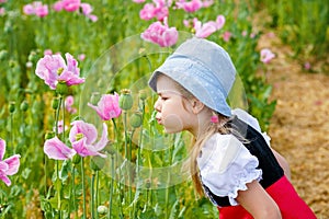 Little preschool girl in poppy field. Cute happy child in red riding hood dress play outdoor on blossom flowering meadow