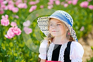 Little preschool girl in poppy field. Cute happy child in red riding hood dress play outdoor on blossom flowering meadow