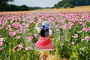 Little preschool girl in poppy field. Cute happy child in red riding hood dress play outdoor on blossom flowering meadow