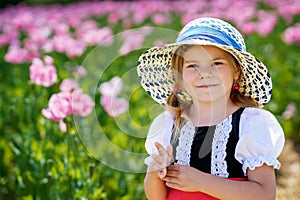 Little preschool girl in poppy field. Cute happy child in red riding hood dress play outdoor on blossom flowering meadow