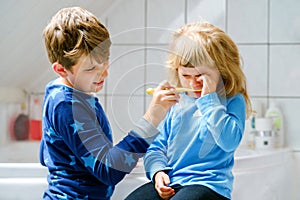 Little preschool girl and preteen school boy brushing teeth. Brother teaching sister brush teeth. Sad upset crying child