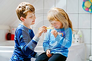 Little preschool girl and preteen school boy brushing teeth. Brother teaching sister brush teeth. Sad upset crying child