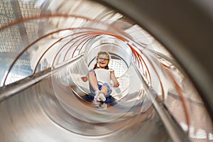 Little preschool girl riding from childrens slides on playground. Happy smiling child having fun in game center for kids