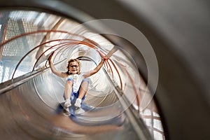 Little preschool girl riding from childrens slides on playground. Happy smiling child having fun in game center for kids