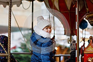 Little preschool girl riding on a merry go round carousel horse at Christmas funfair or market, outdoors. Happy child
