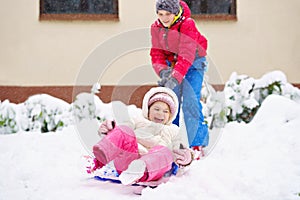 Little preschool girl and school boy playing with snow in winter. Brother sliding cute sister on shovel. Happy smiling