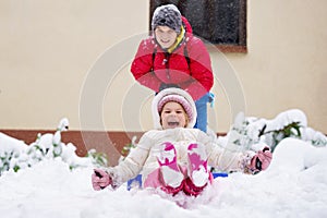 Little preschool girl and school boy playing with snow in winter. Brother sliding cute sister on shovel. Happy smiling