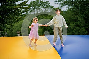 Little preschool girl and school sister jumping on trampoline. Happy funny children, siblings in love having fun with photo