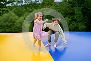 Little preschool girl and school sister jumping on trampoline. Happy funny children, siblings in love having fun with photo