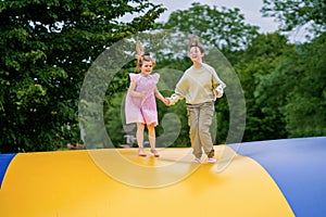 Little preschool girl and school sister jumping on trampoline. Happy funny children, siblings in love having fun with outdoor photo