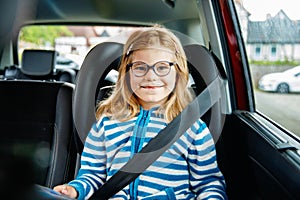 Little Preschool Girl Sitting in Her Car Seat. Happy Child with Eyeglasses Reading a Book, Smiling on the Way to Family