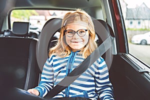 Little Preschool Girl Sitting in Her Car Seat. Happy Child with Eyeglasses Reading a Book, Smiling on the Way to Family