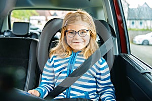 Little Preschool Girl Sitting in Her Car Seat. Happy Child with Eyeglasses Reading a Book, Smiling on the Way to Family