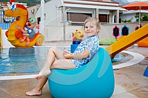 Little preschool girl sitting by outdoor swimming pool in hotel resort. Child learning to swim in outdoor pool