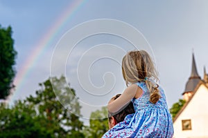 Little preschool girl sitting on shoulder of father. Happy toddler child and man observing rainbow on sky after