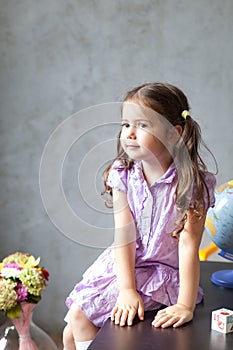 Little preschool girl sitting on a table with textbooks and a globe