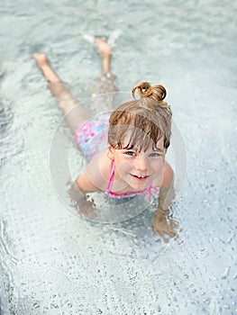 Little preschool girl splashing in an outdoor swimming pool on warm summer day. Happy healthy toddler child enjoying