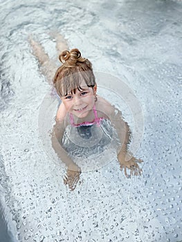 Little preschool girl splashing in an outdoor swimming pool on warm summer day. Happy healthy toddler child enjoying