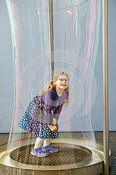 Little preschool girl standing inside a huge soap bubble. Happy girl having fun.