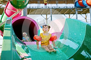 Little preschool girl on water slide in aqua park. Happy child having fun on water slides on family summer vacation in