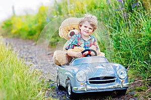 Little preschool kid boy driving big toy car and having fun with playing with his plush toy bear, outdoors. Child