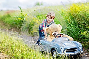 Little preschool kid boy driving big toy car and having fun with playing with his plush toy bear, outdoors. Child