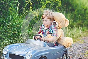 Little preschool kid boy driving big toy car and having fun with playing with his plush toy bear, outdoors. Child