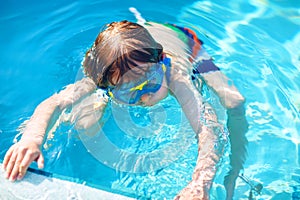 Little preschool kid boy making swim competition sport. Kid with swimming goggles reaching edge of the pool . Child