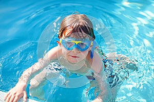 Little preschool kid boy making swim competition sport. Kid with swimming goggles reaching edge of the pool . Child