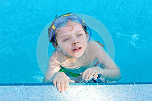 Little preschool kid boy making swim competition sport. Kid with swimming goggles reaching edge of the pool . Child