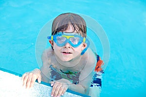 Little preschool kid boy making swim competition sport. Kid with swimming goggles reaching edge of the pool . Child