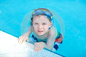 Little preschool kid boy making swim competition sport. Kid with swimming goggles reaching edge of the pool . Child