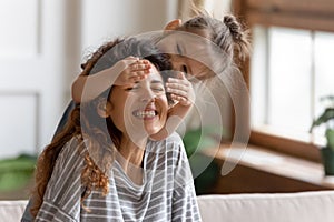 Little preschool kid daughter covering eyes of laughing mother.