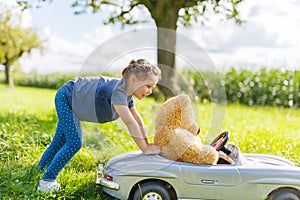 Little preschool kid girl driving big toy car and having fun with playing with big plush toy bear
