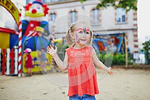 Little preschooler girl with butterfly face painting outdoors