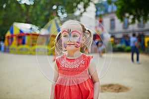 Little preschooler girl with butterfly face painting outdoors