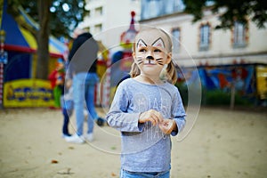 Little preschooler girl with cat face painting, making funny grimace outdoors photo