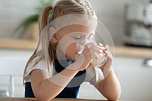Little preschooler girl drink milk from glass at home