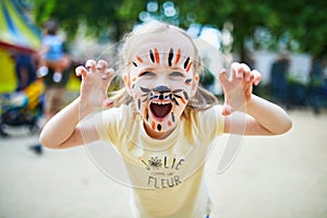 Little preschooler girl with tiger face painting outdoors photo