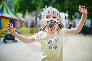 Little preschooler girl with tiger face painting outdoors photo