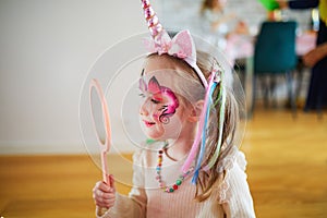 Little preschooler girl in unicorn costume admiring her facepaint on a birthday party